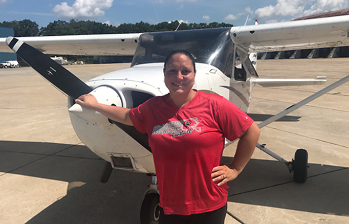 Student standing in front of an airplane on the run way.