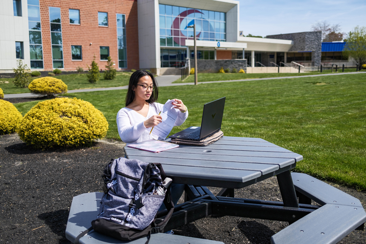 Student studying on outside picnic table with papers and laptop