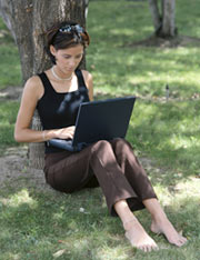 female student sitting under tree working with laptop