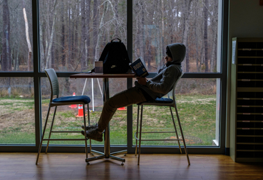 A student seated, reading a book, in the Student Center